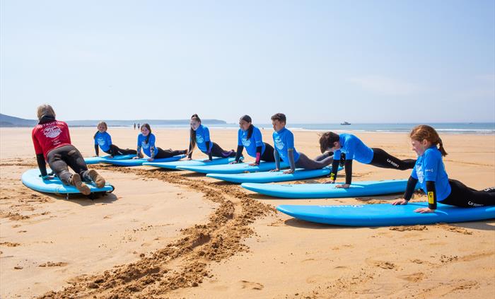 Group of children practising surf skills on the beach with a Blue Horizons instructor during a surf lesson in Pembrokeshire.